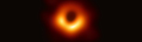 Die erste Abbildung eines schwarzen Lochs. Ein sehr unscharfer, orangener Lichtring vor schwarzem Hintergrund. Die untere Hälfte des Rings ist breiter und gelber als die obere Hälfte.